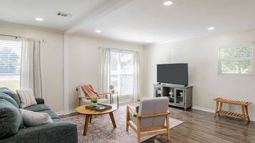 Una sala moderna con un sofá, un sillón, una mesa de centro y un televisor sobre un mueble.
