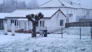 Un immeuble résidentiel dont le toit est recouvert de neige, avec une cour clôturée et un arbre au premier plan.
