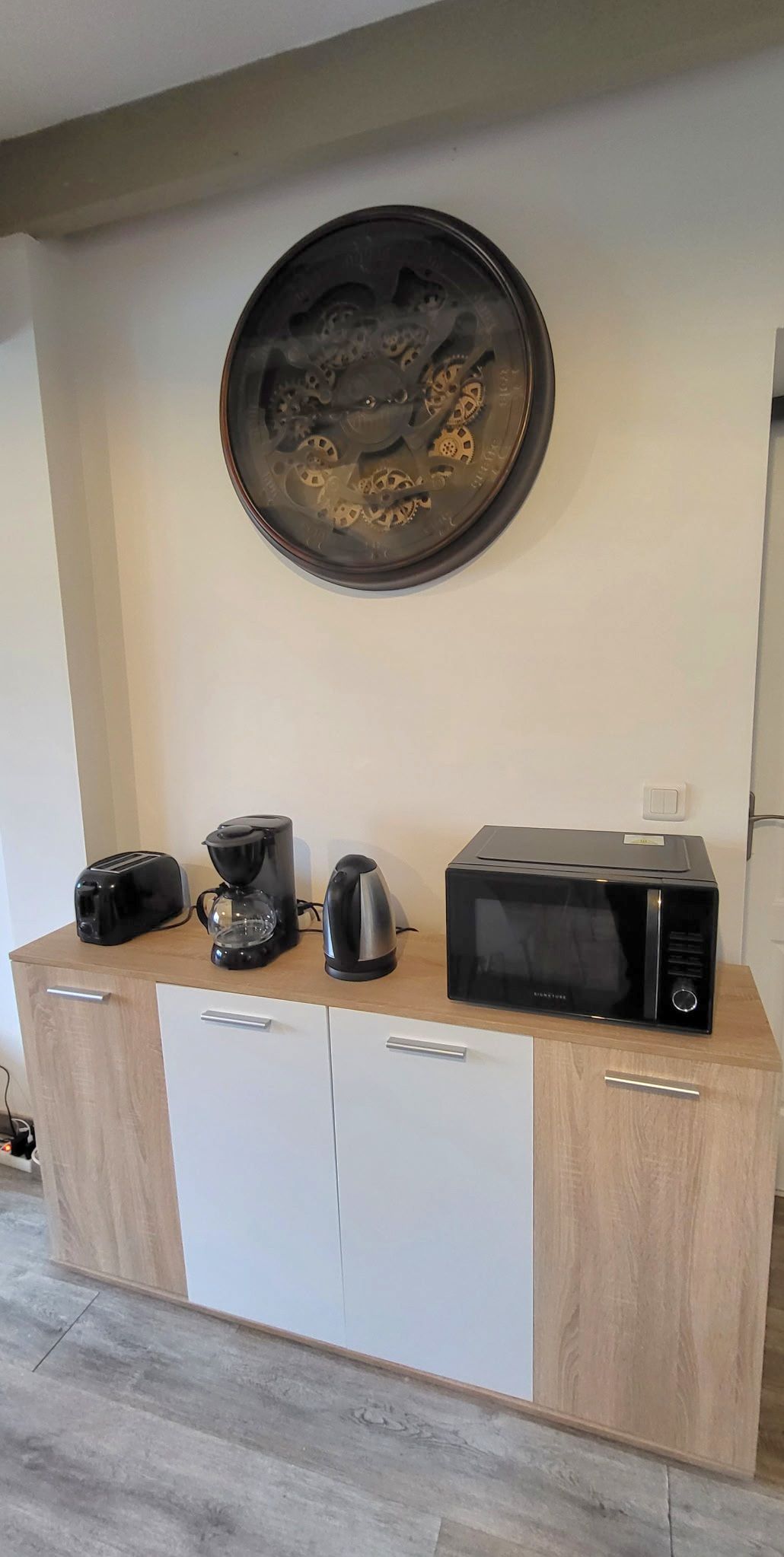 A kitchen area with a microwave, toaster, and coffee maker on a wooden cabinet.