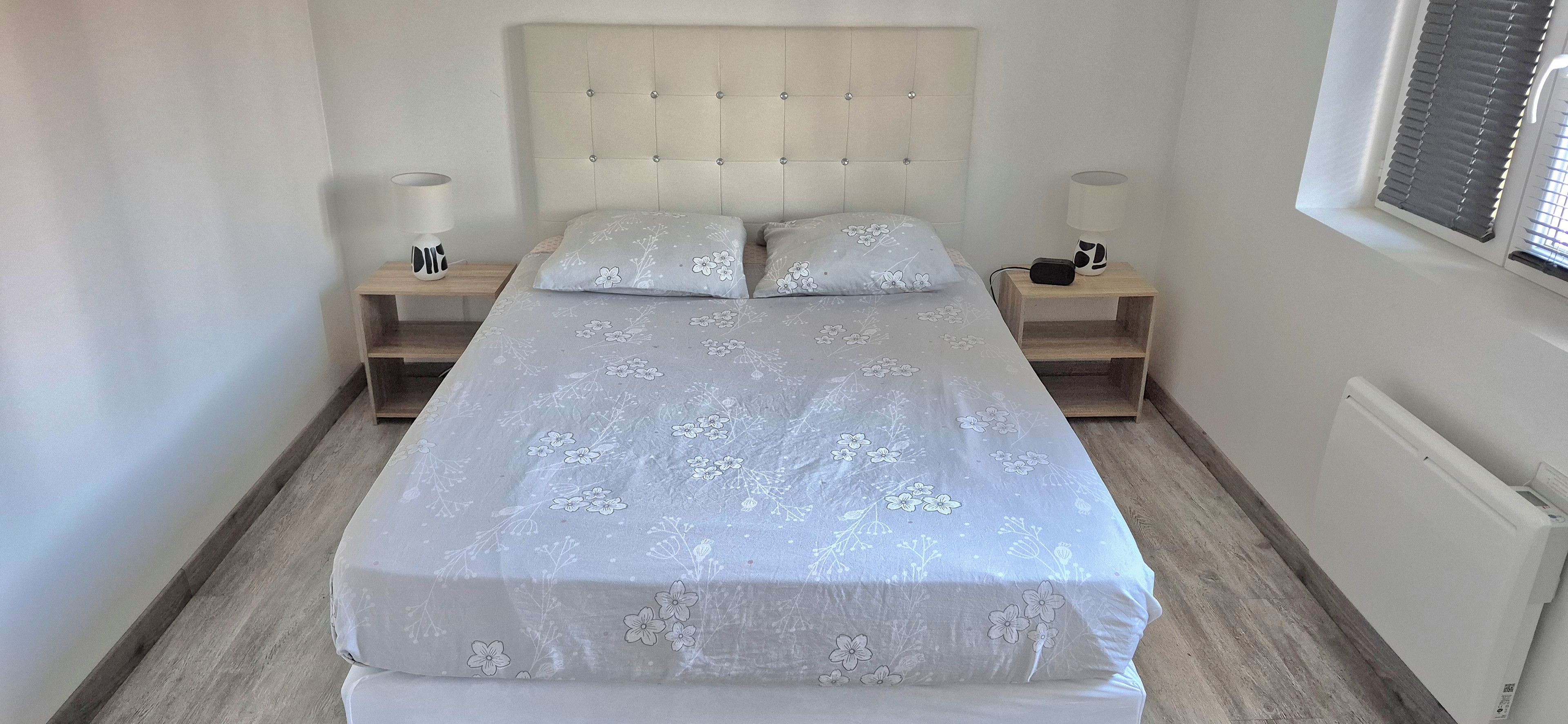 Un dormitorio con una cama, dos mesitas de noche y un ventanal con persianas.