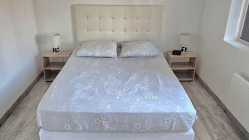 Un dormitorio con una cama, dos mesitas de noche y un ventanal con persianas.