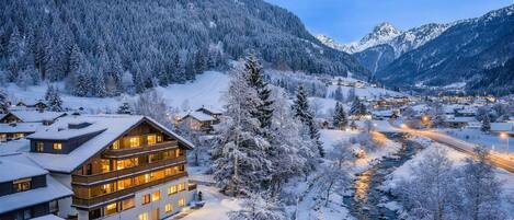 A multi-story hotel with a snow-covered landscape, a river, and mountains in the background.