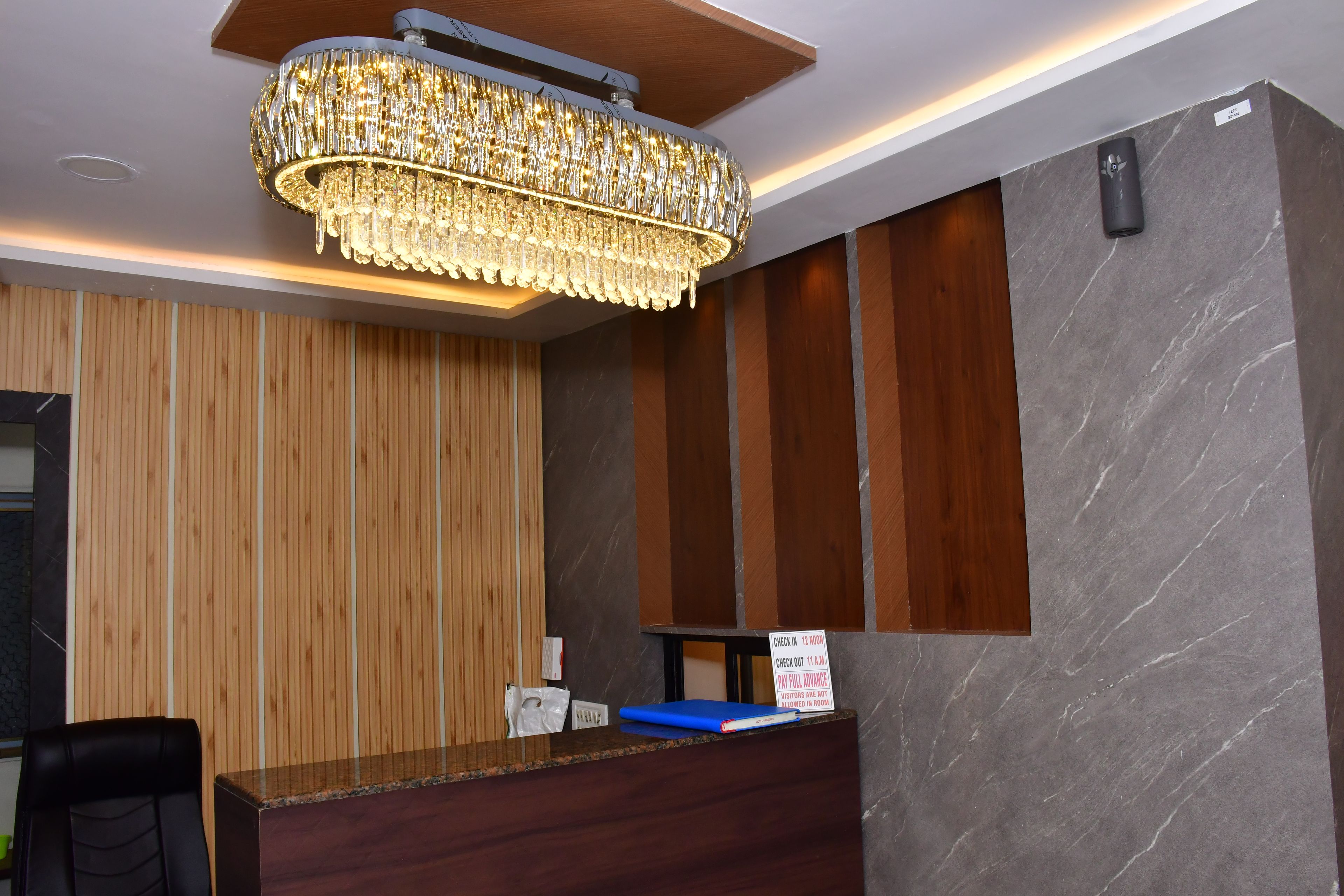 A hotel reception area with a wooden panel wall, a marble wall, and a chandelier.