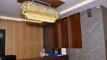 A hotel reception area with a wooden panel wall, a marble wall, and a chandelier.