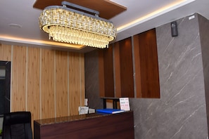 A hotel reception area with a wooden panel wall, a marble wall, and a chandelier.