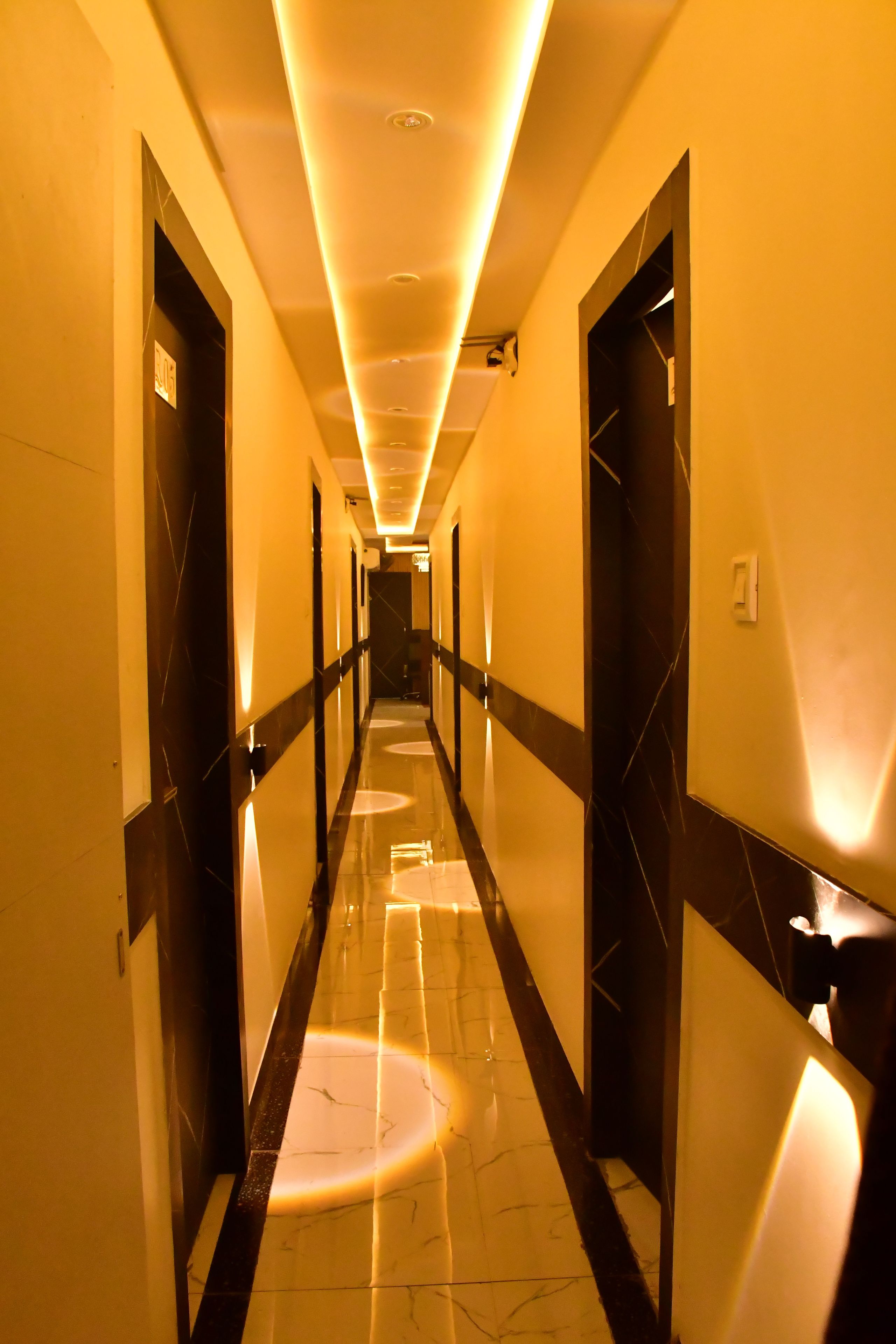 A hotel corridor with a reflective floor, doors on both sides, and overhead lighting.