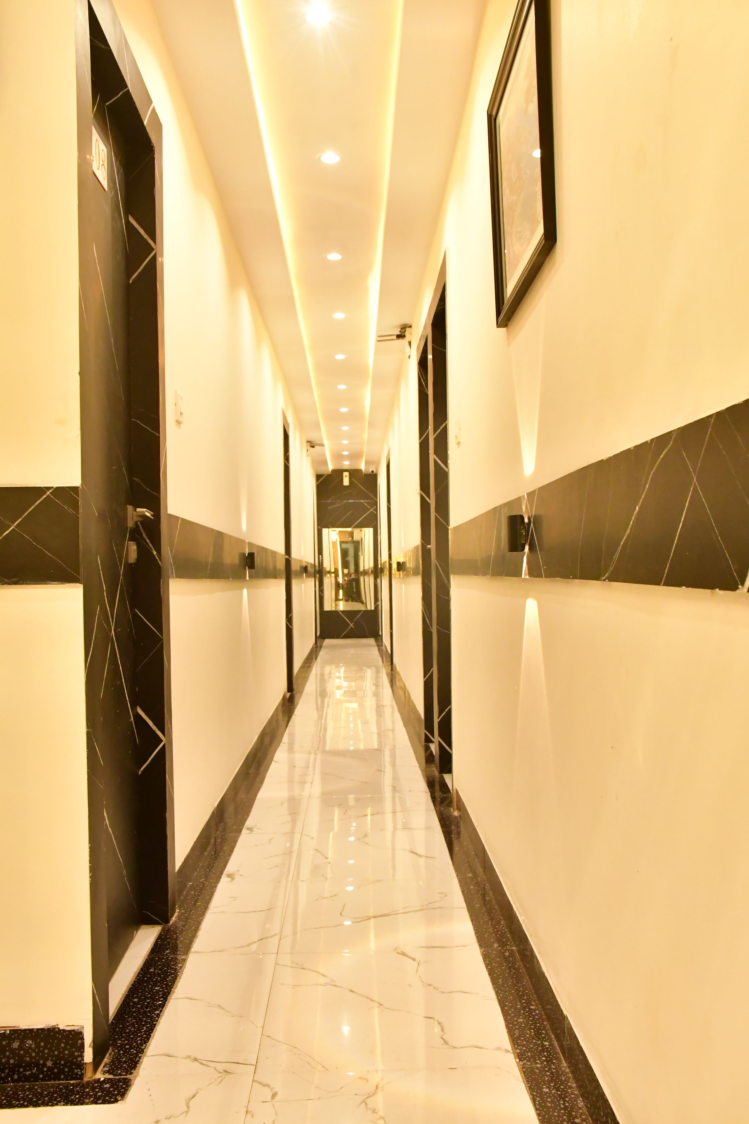 Un pasillo de hotel con suelo de mármol, paredes blanco y negro e iluminación empotrada.