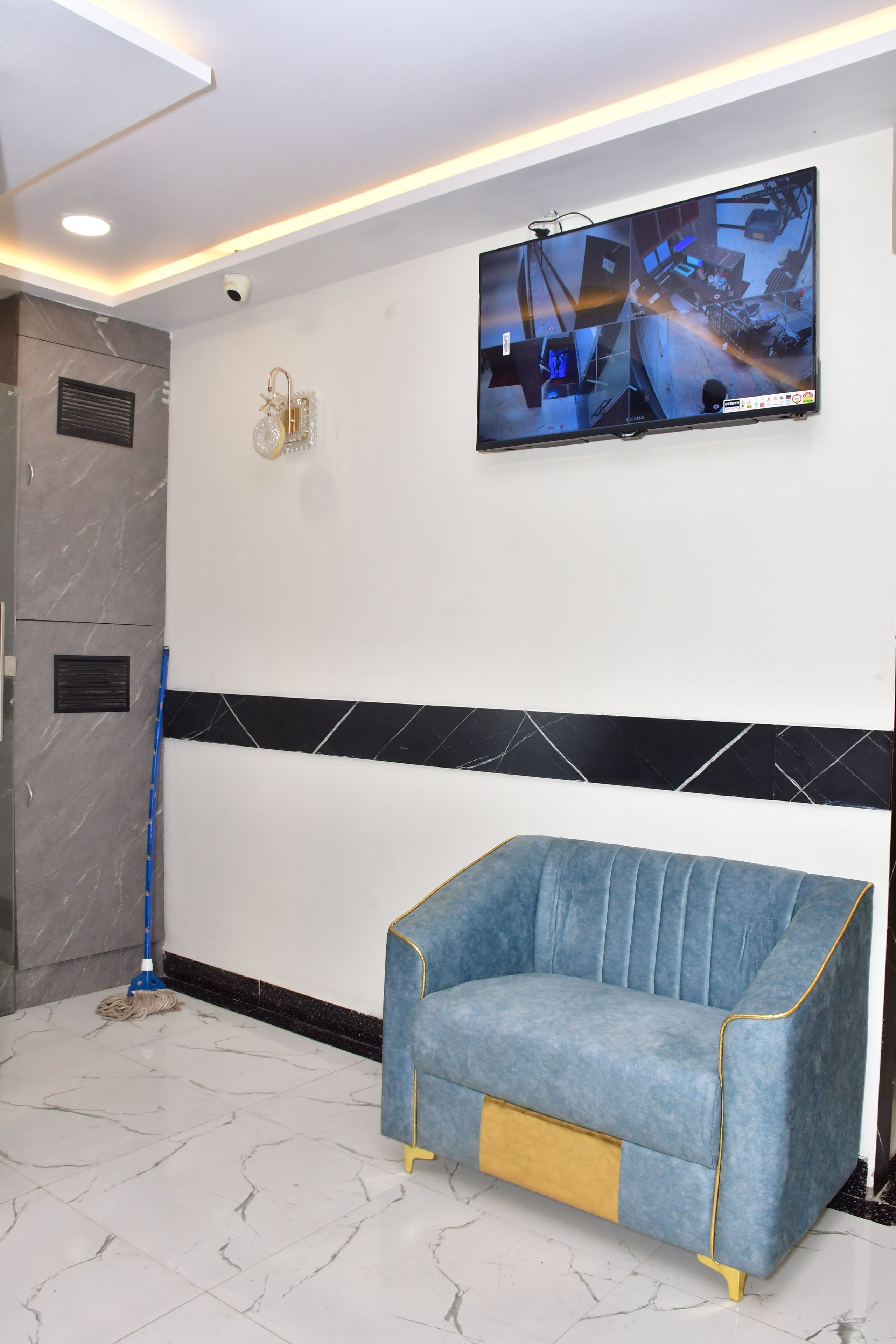 A modern waiting area with a blue sofa, a mounted security camera, and a flat-screen TV displaying surveillance footage.