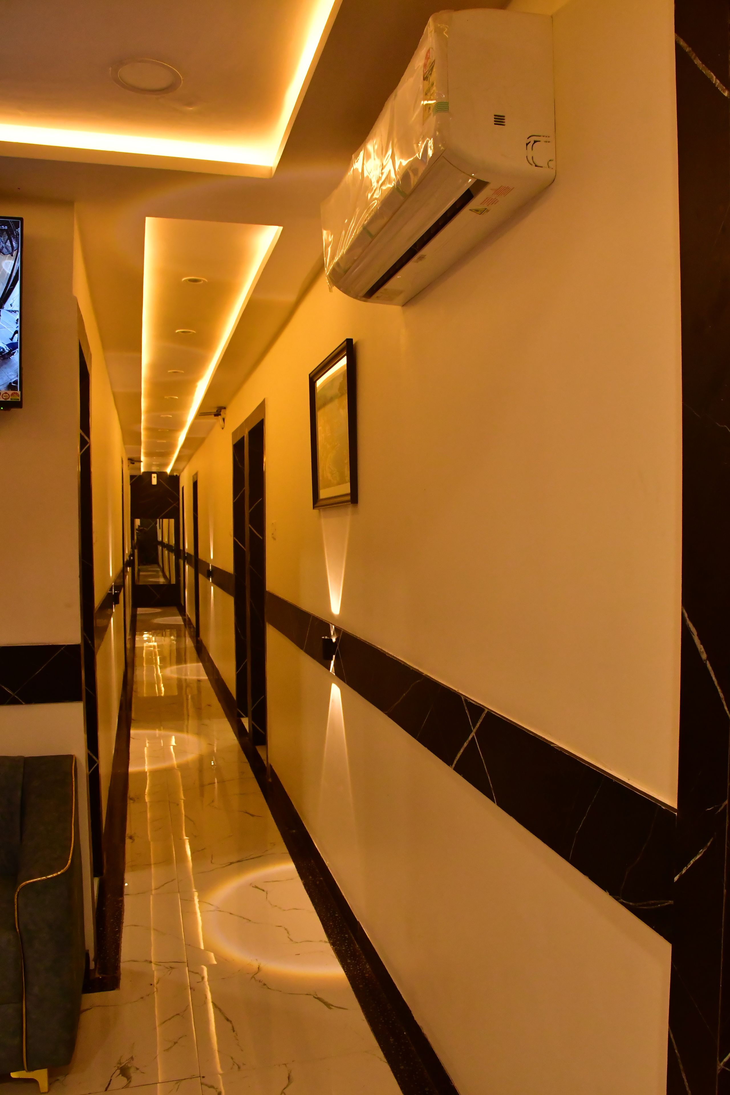A hotel corridor with a long, straight layout, air conditioning units, and framed artwork on the walls.