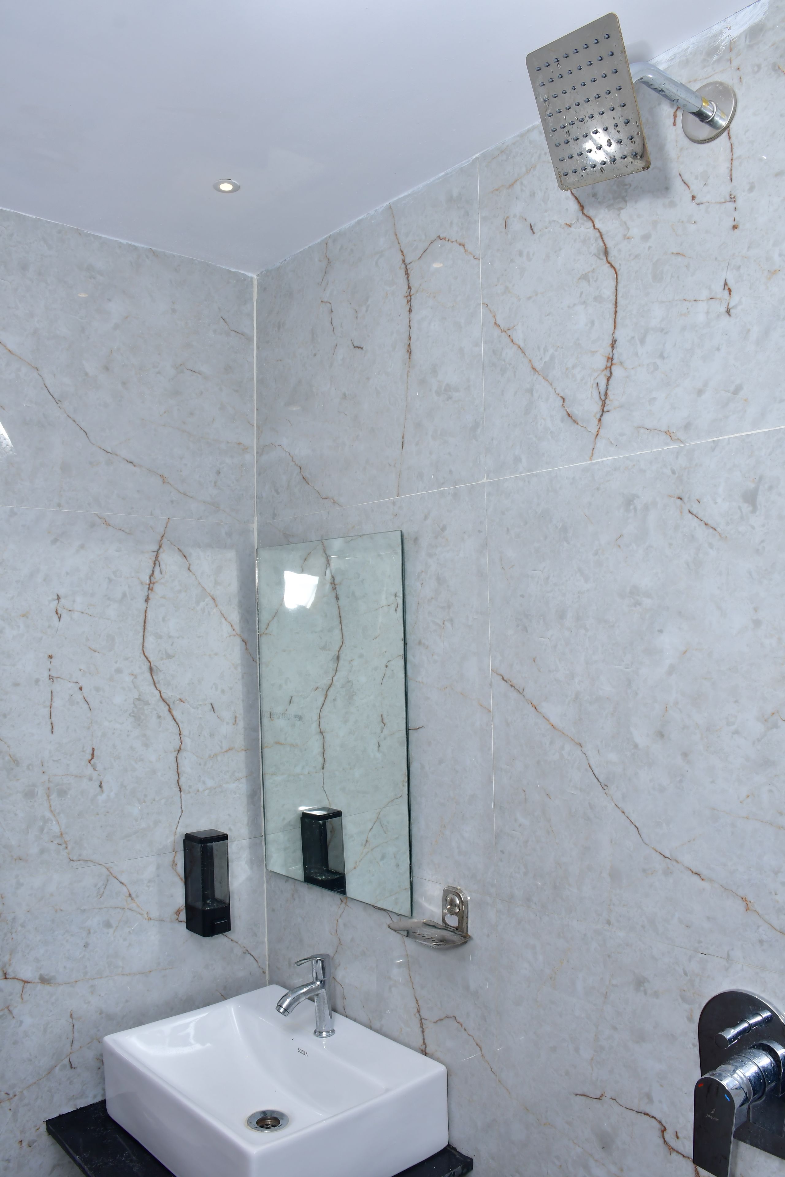 Un bagno con un lavandino bianco, uno specchio e un soffione doccia.