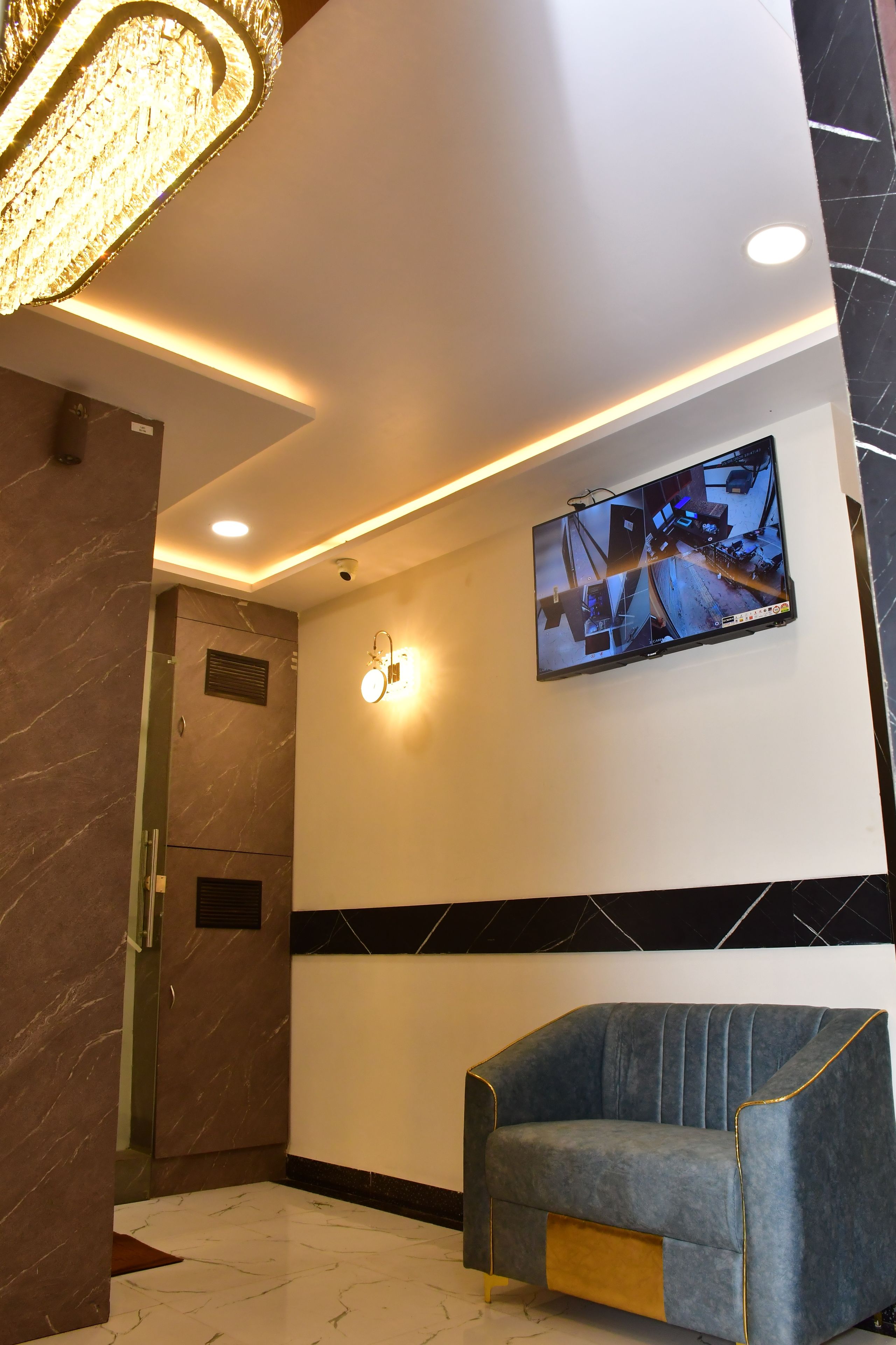 A lobby with a modern design, featuring a seating area, a mounted security camera, and a wall-mounted television displaying a surveillance feed.