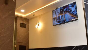 A lobby with a modern design, featuring a seating area, a mounted security camera, and a wall-mounted television displaying a surveillance feed.