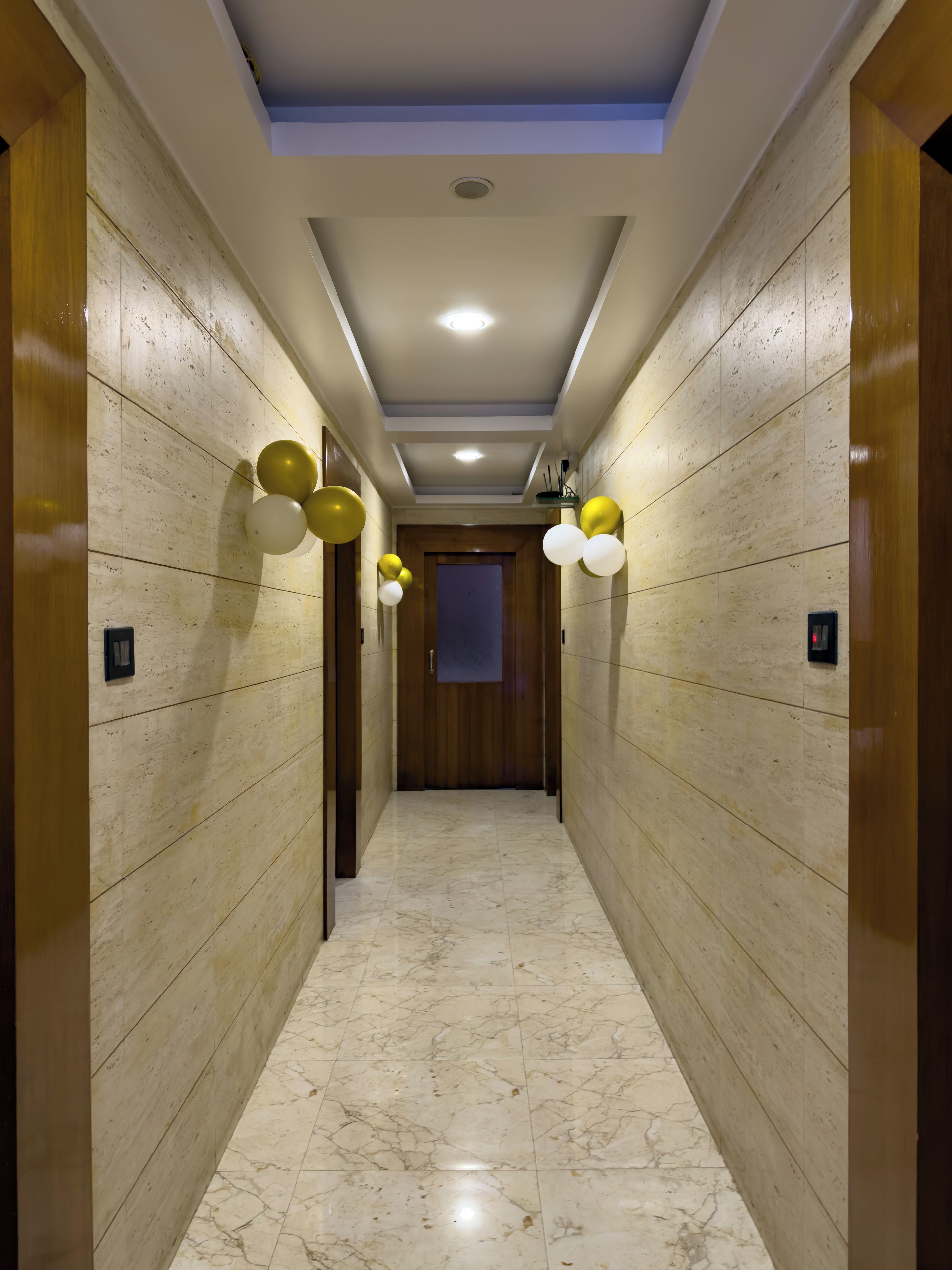 A hallway with marble flooring and wooden panel walls, leading to a door with a frosted glass panel.