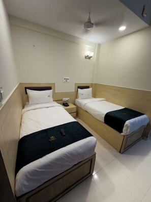 A hotel room with two single beds, a bedside table with a phone, and a wall-mounted light fixture. - Hotel Elmont, Near EGL, Domlur (Bengaluru)