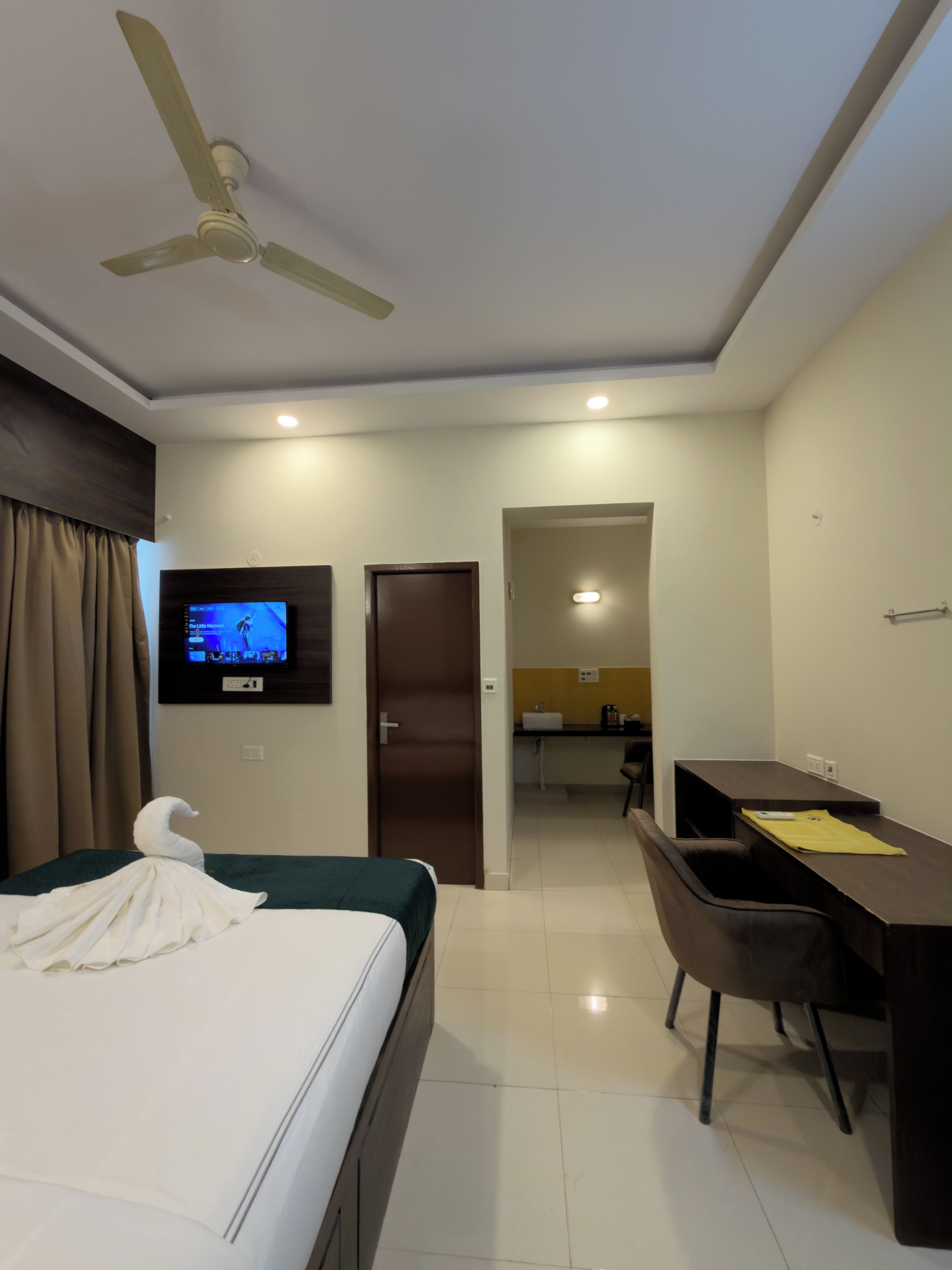 A hotel room with a bed, a desk, a chair, a television, and a ceiling fan.