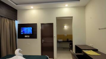 A hotel room with a bed, a desk, a chair, a television, and a ceiling fan.