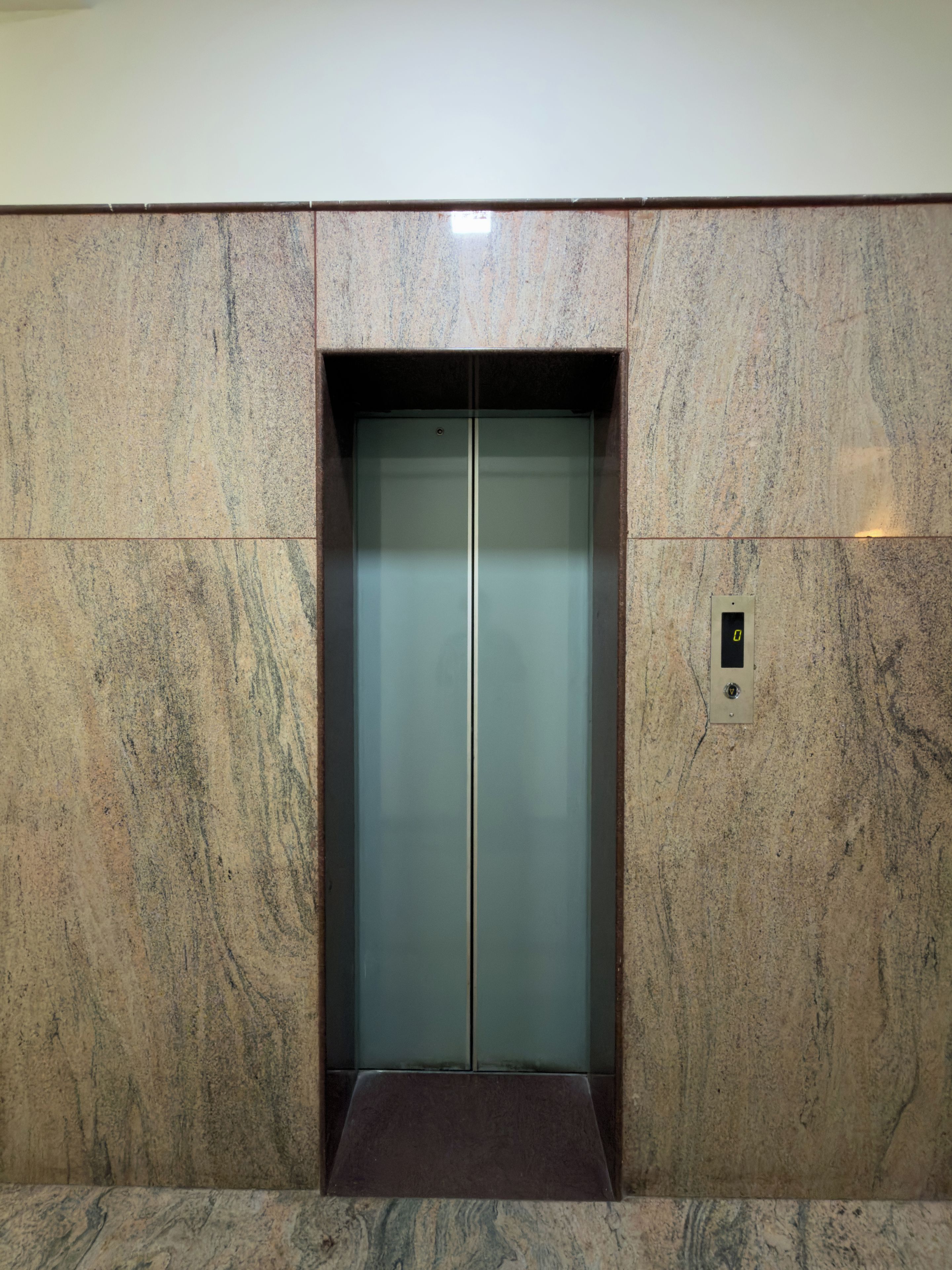 An elevator with a metallic finish, set in a wall with a textured surface.