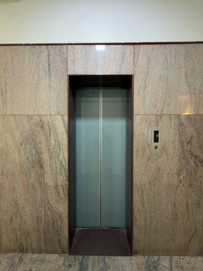 An elevator with a metallic finish, set in a wall with a textured surface. - Hotel Elmont, Near EGL, Domlur (Bengaluru)