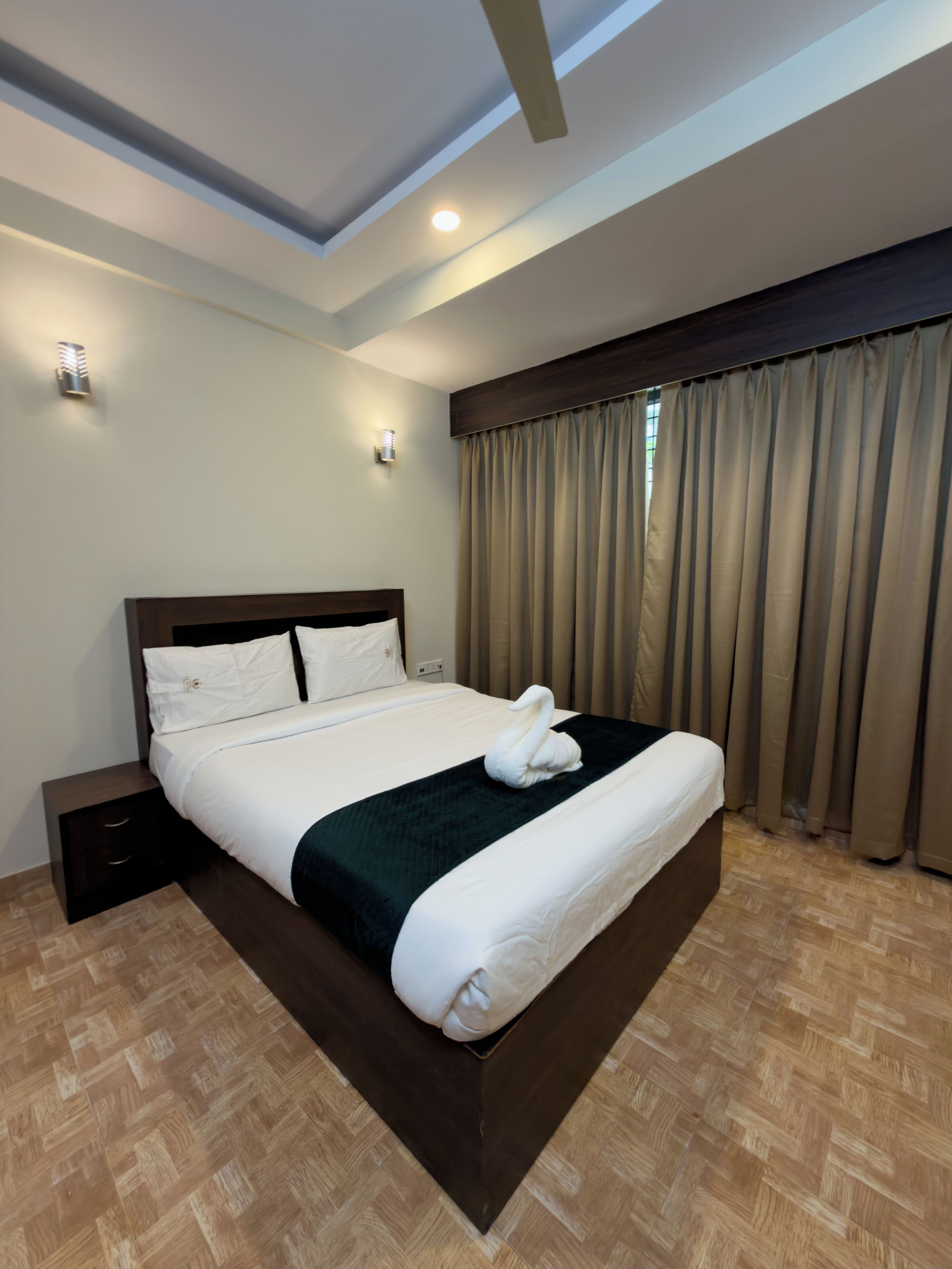 A hotel room with a large bed, a nightstand, a wall-mounted light, and a window with curtains.