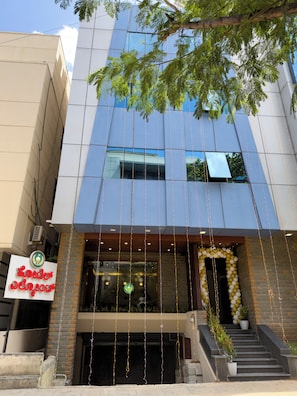 A modern building with a glass facade, a signboard, and a decorative archway with balloons. - Hotel Elmont, Near EGL, Domlur (Bengaluru)