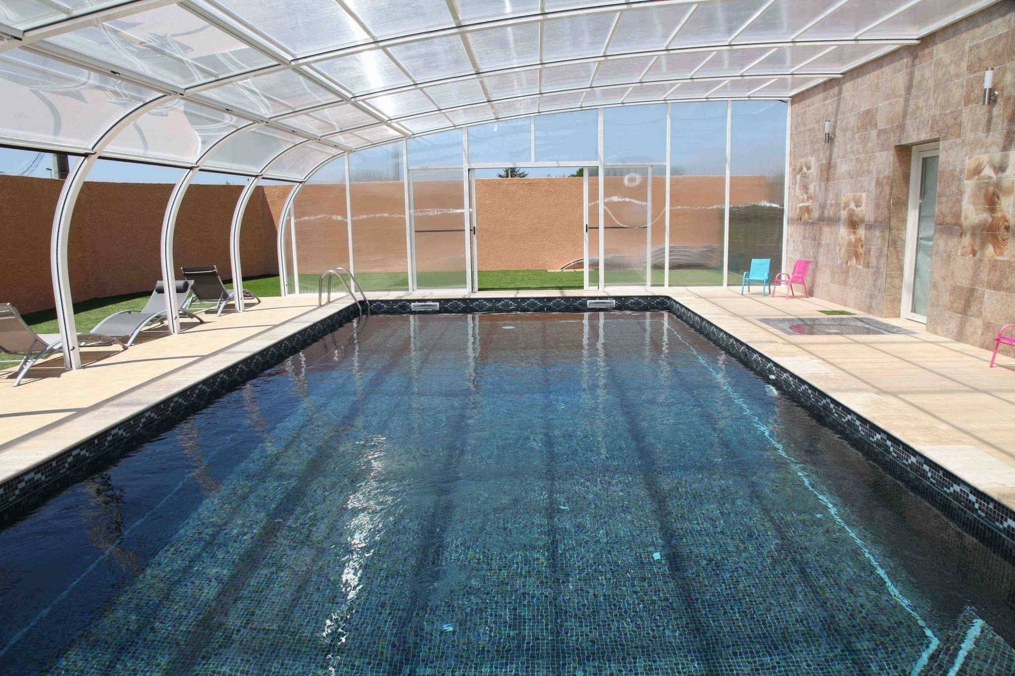 A swimming pool with a glass enclosure, surrounded by lounge chairs and a view of the landscape.