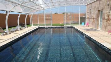A swimming pool with a glass enclosure, surrounded by lounge chairs and a view of the landscape.