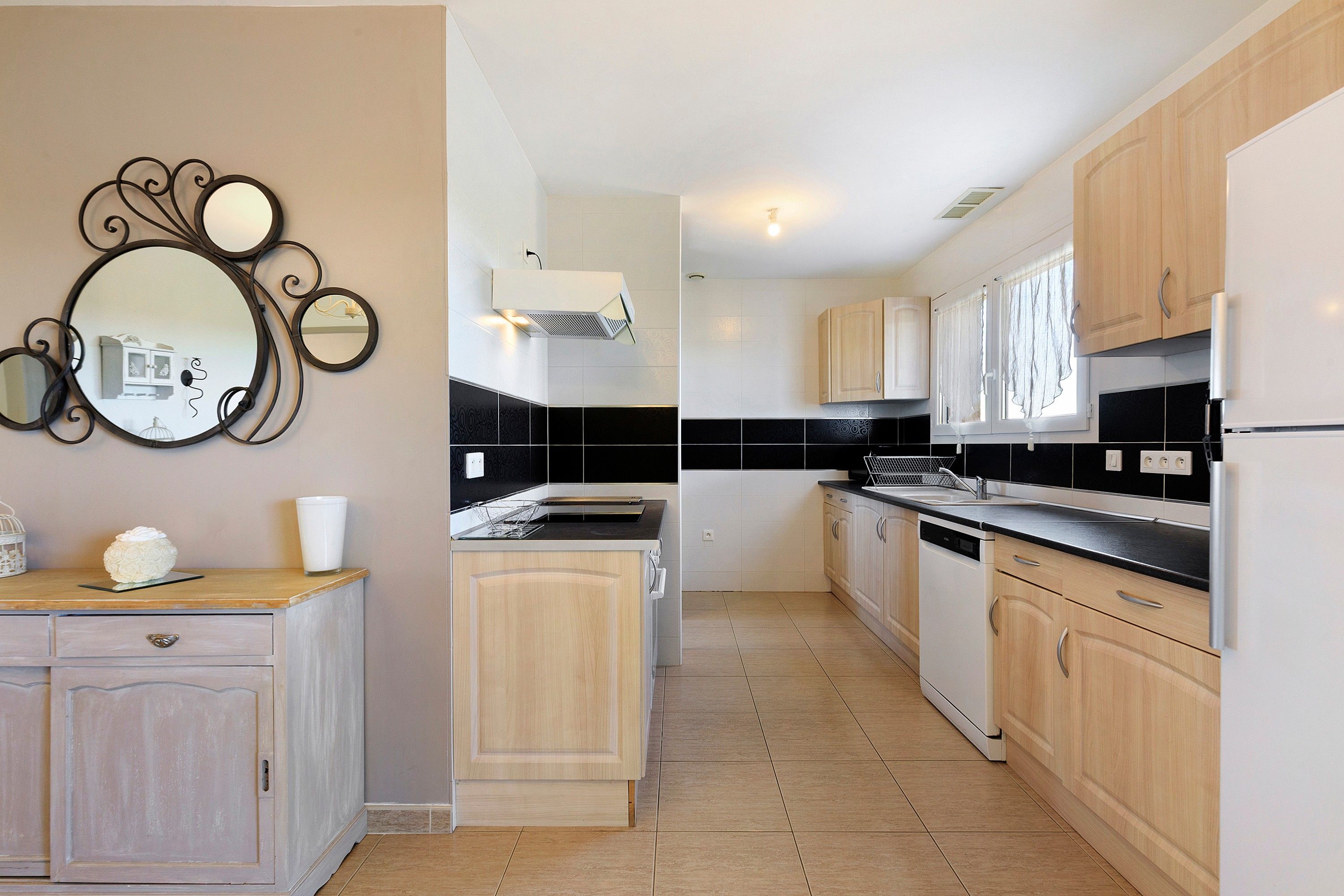A modern kitchen with light wood cabinets, a black countertop, and a built-in oven.