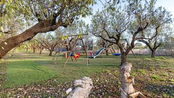 A playground with swings, slides, and climbing structures surrounded by trees and a grassy area.