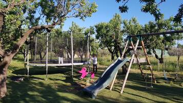 An outdoor playground with a slide, swings, and a trampoline.