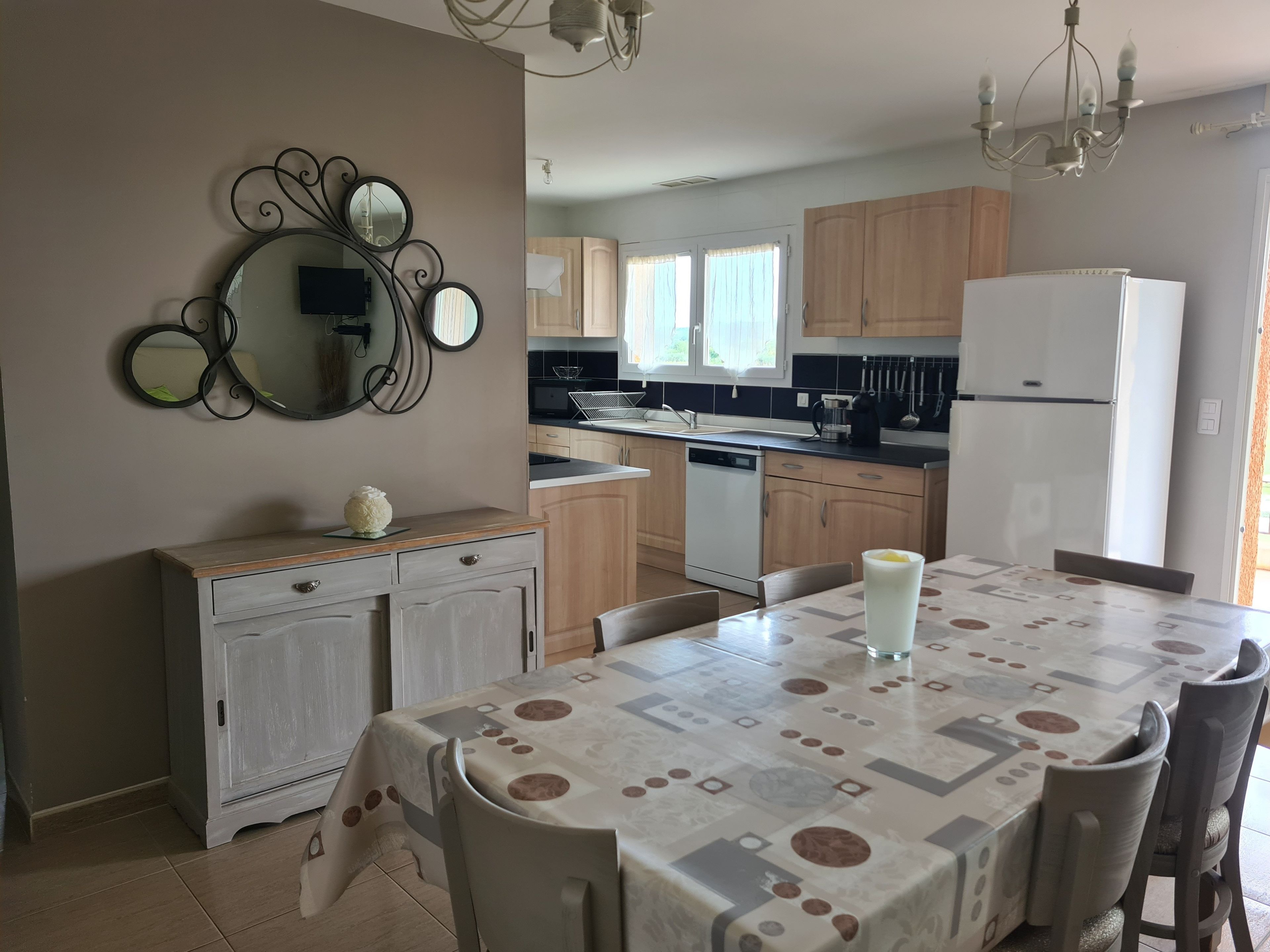 Una cocina moderna con armarios de madera, un refrigerador blanco y una mesa de comedor con mantel estampado.