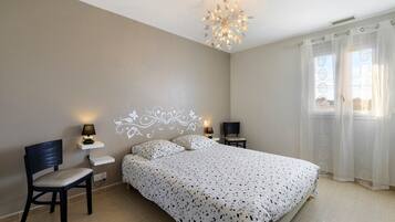 A bedroom with a bed, two bedside tables with lamps, a chair, a decorative ceiling light, and a window with curtains.