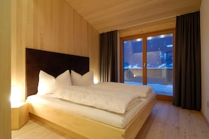 A wooden bed with white bedding in a room with wooden walls and a large window. - Chalet With Fireplace and Balcony (Gaschurn)
