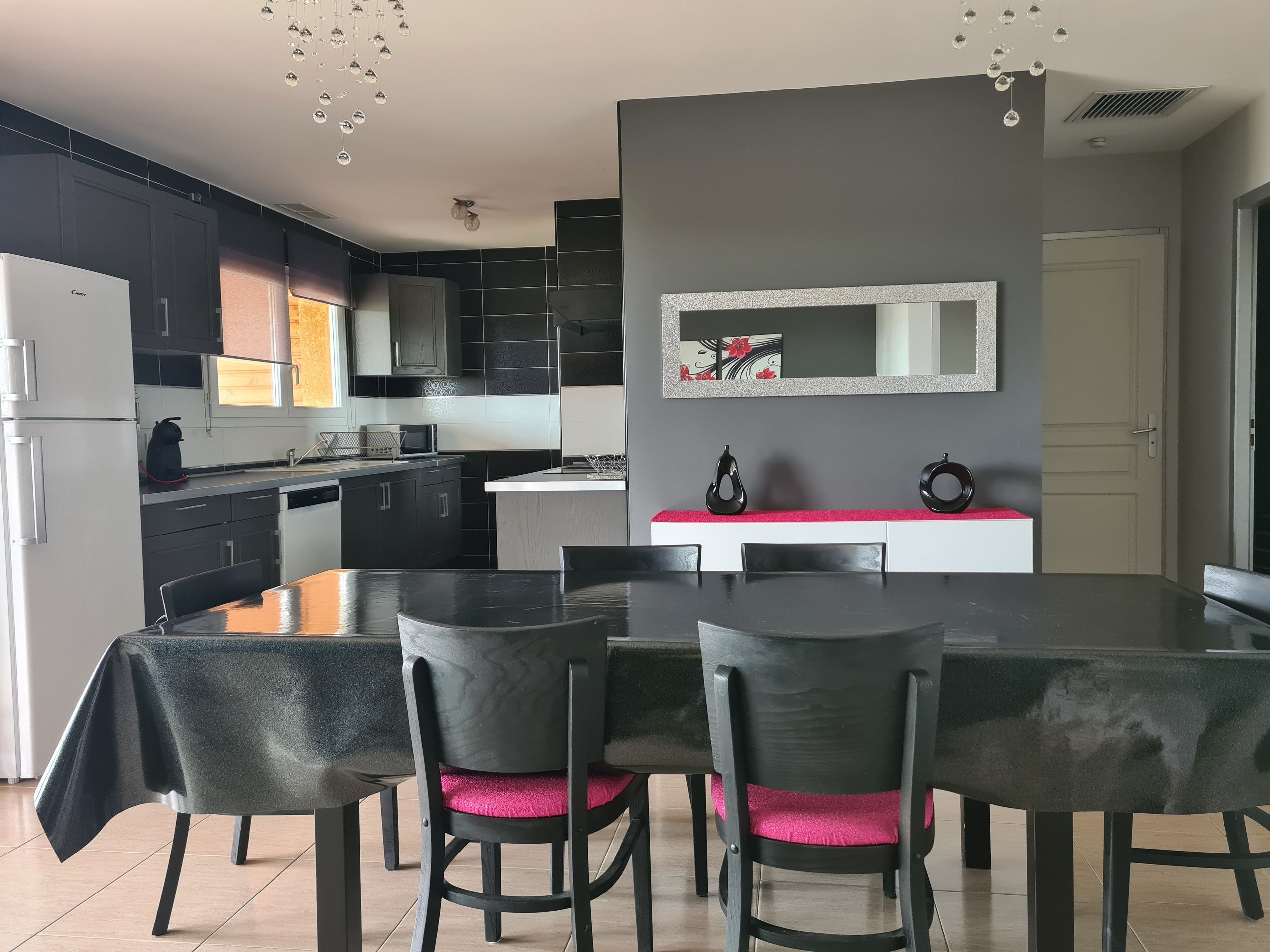 A modern kitchen with dark cabinetry, a central island, and a dining area with a table and chairs.