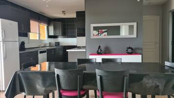 A modern kitchen with dark cabinetry, a central island, and a dining area with a table and chairs.
