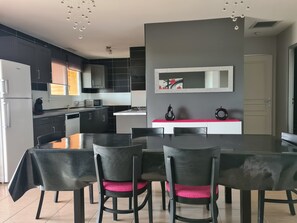 Cocina moderna con armarios oscuros, una isla central y una zona de comedor con mesa y sillas.