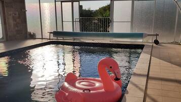 An indoor swimming pool with a clear glass ceiling, a swan inflatable float, and a view of the outdoors.
