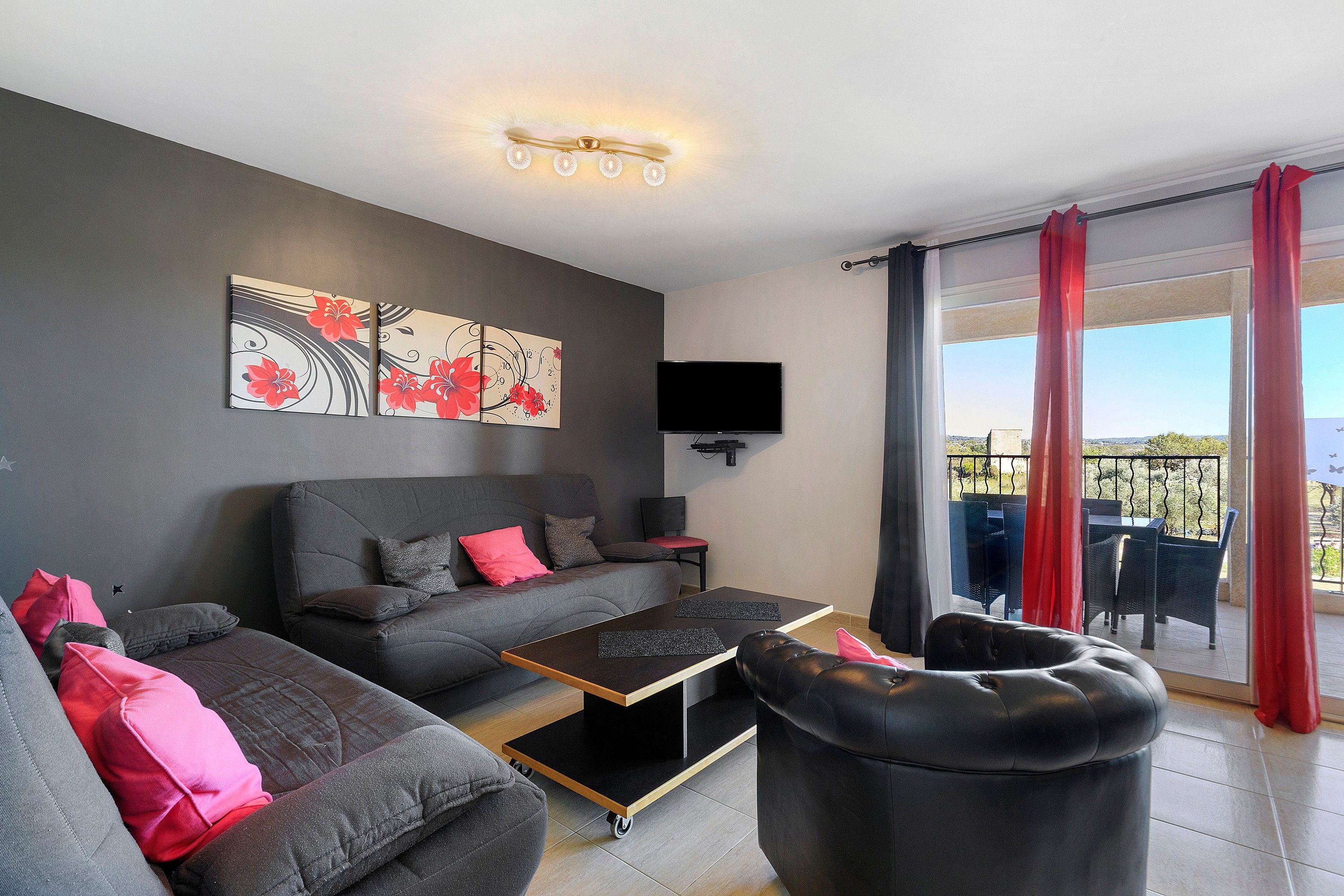 A modern living room with a grey sofa, a black ottoman, a coffee table, and a flat-screen TV mounted on the wall.