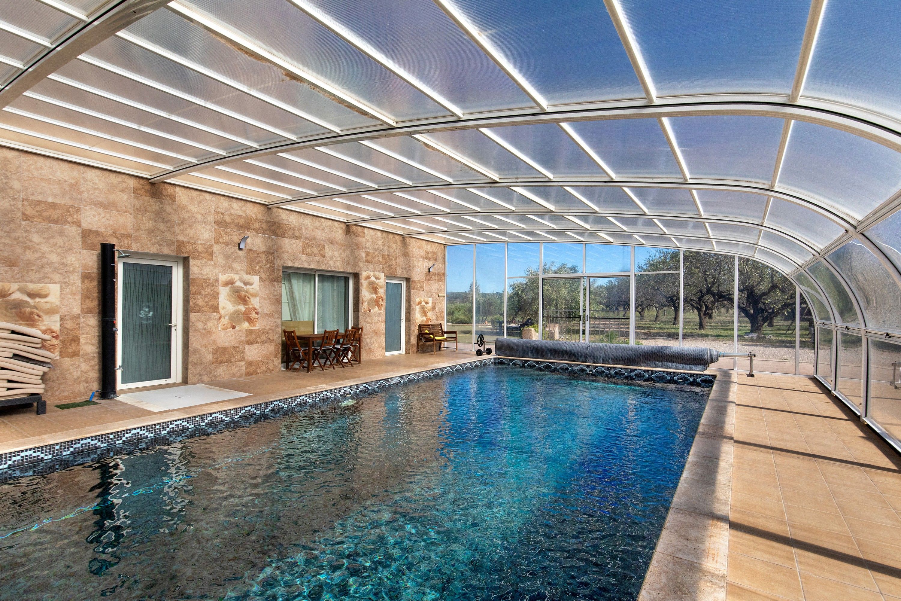 A covered swimming pool with clear water, a tiled deck, and a view of the outdoors.