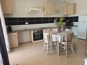 A modern kitchen with wooden cabinets, a built-in oven, a microwave, and a dining table with chairs. - Apartment 'La Valencianne' with Wi-Fi and Air Conditioning (Paulhan)