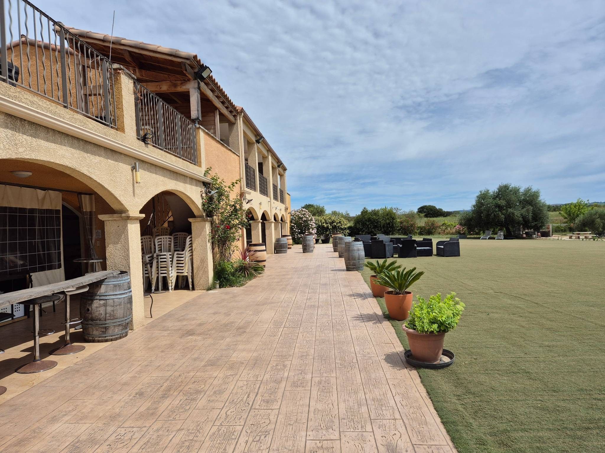 A building with a covered outdoor seating area, a paved walkway, and a grassy field.