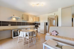 A modern kitchen with a dining area, a refrigerator, and a sofa with a glass coffee table.