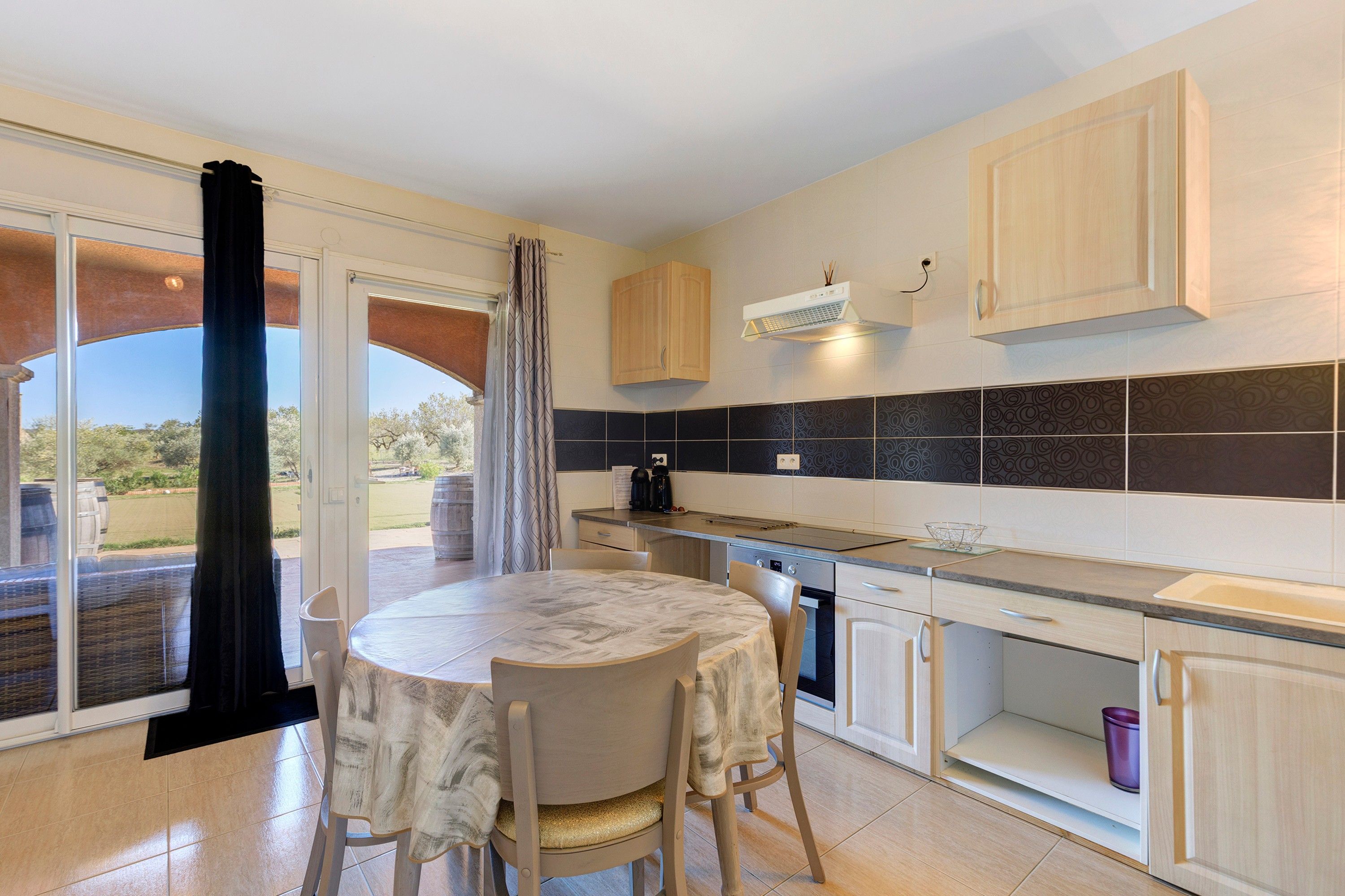 A modern kitchen with a dining area, featuring a large table, chairs, and a view through the sliding glass door.