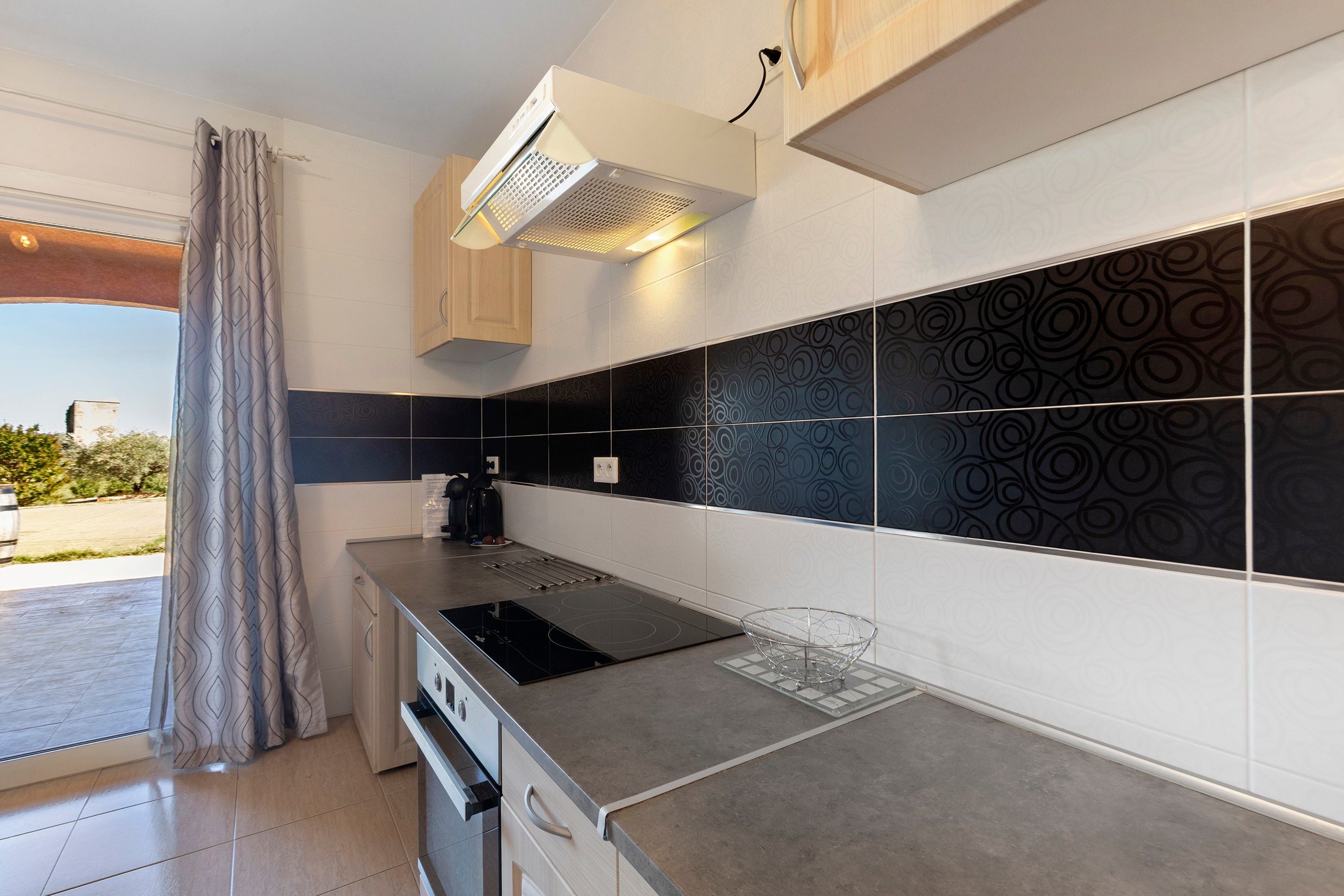 Een moderne keuken met een ingebouwde kookplaat, een waterkoker en een glazen kom op het aanrecht.