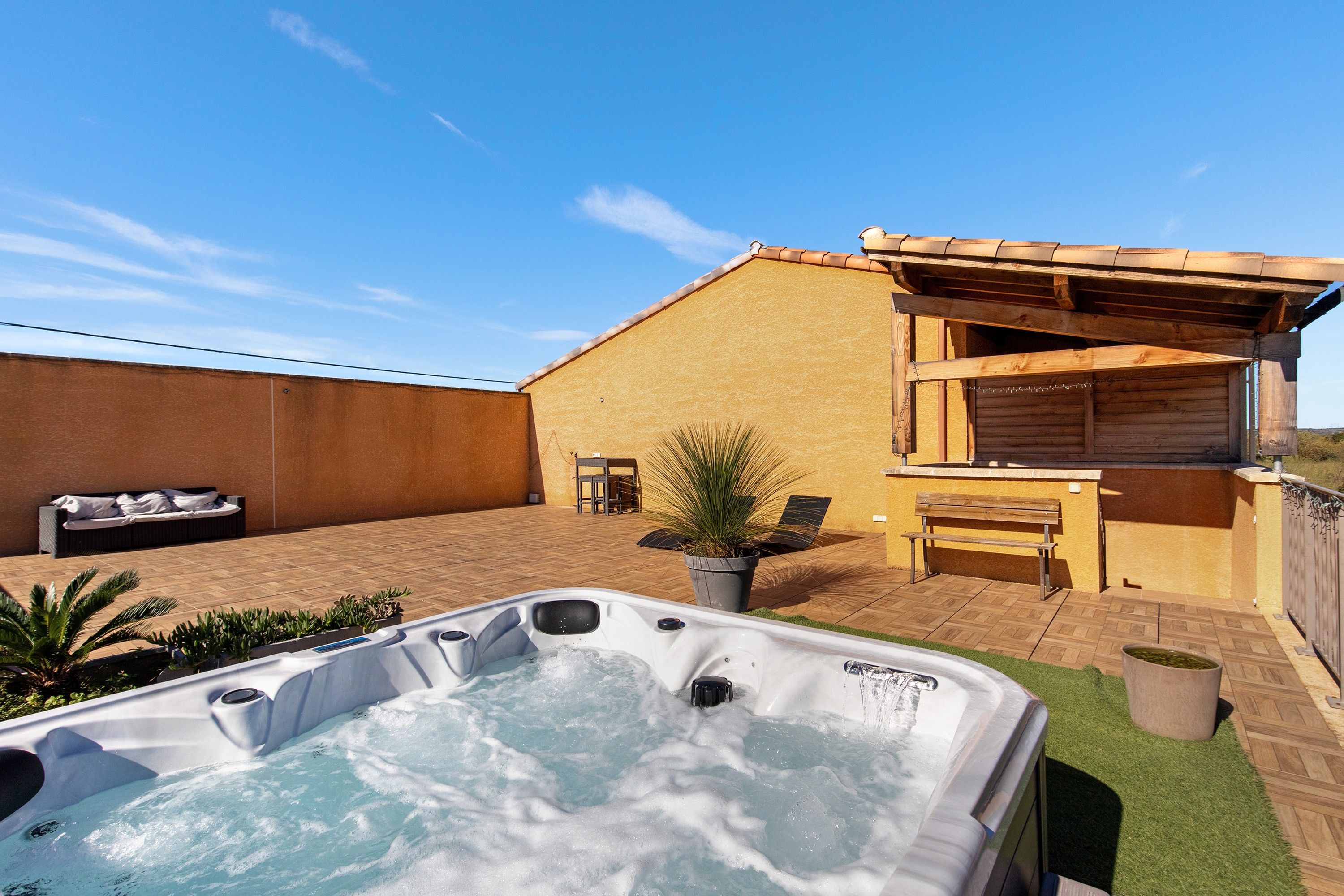 Un jacuzzi en un patio trasero con terraza, una pérgola de madera y un área de estar.