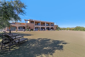 A two-story building with a flat roof, multiple balconies, and a large open grassy area in front.