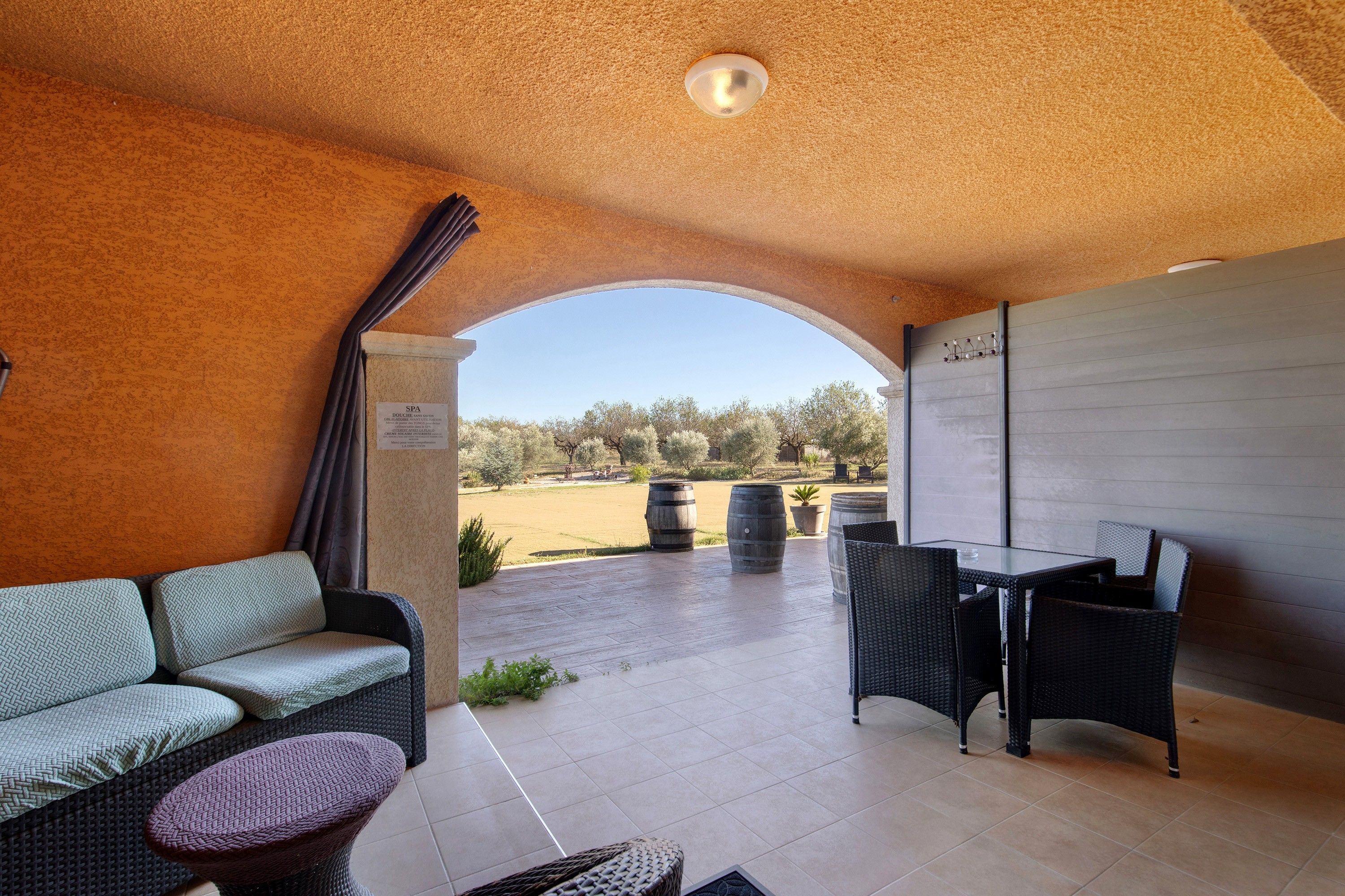 Un espace extérieur aménagé, abrité et doté d’un canapé, de chaises et d’une table, offrant une vue sur un jardin paysager.