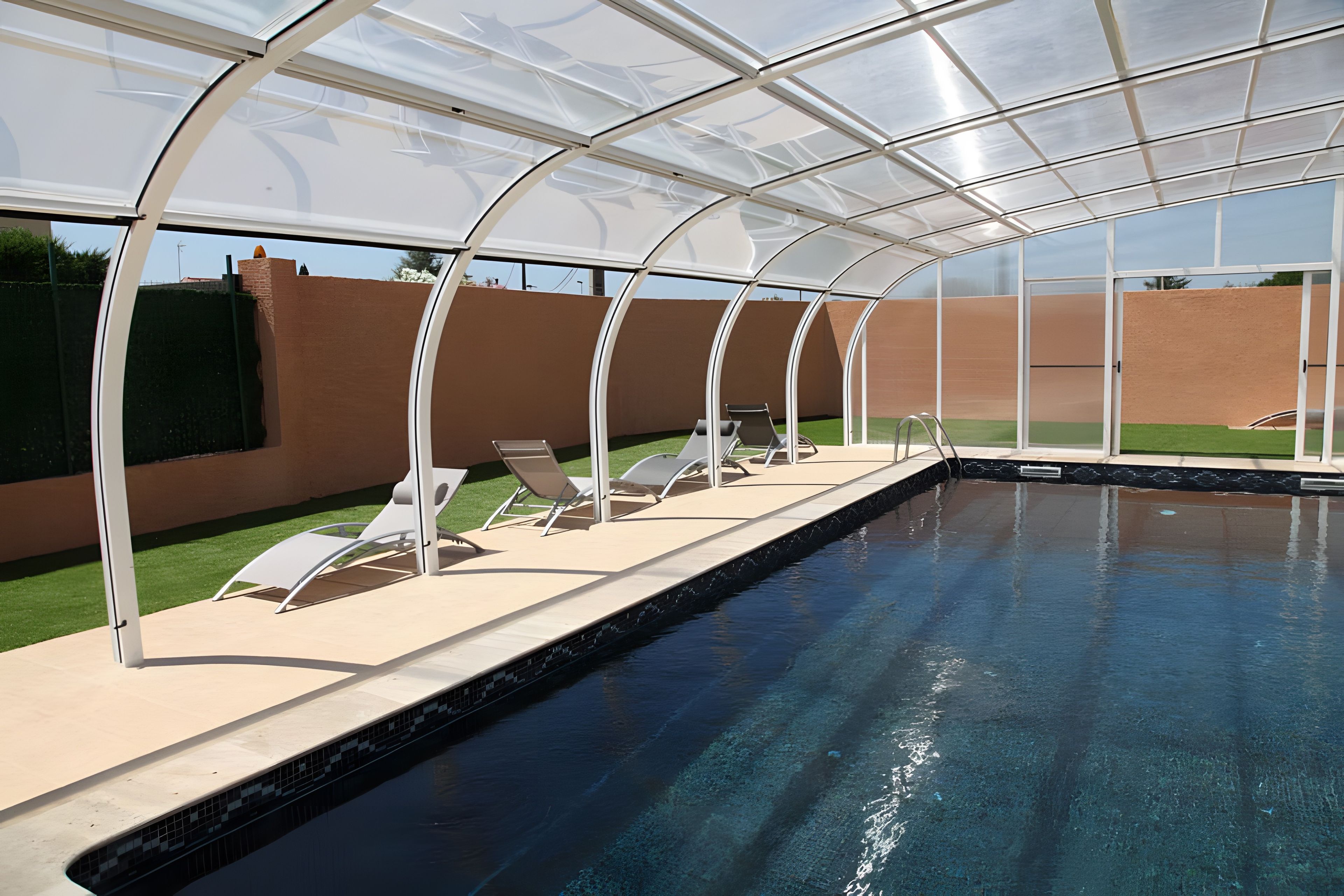 Une piscine dotée d’une enceinte en verre, entourée de chaises longues et d’un mur en briques.