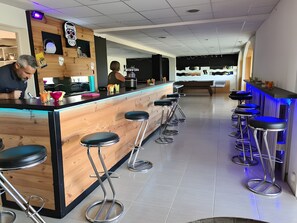 Een bar met krukken, een toonbank en een persoon die erachter werkt.