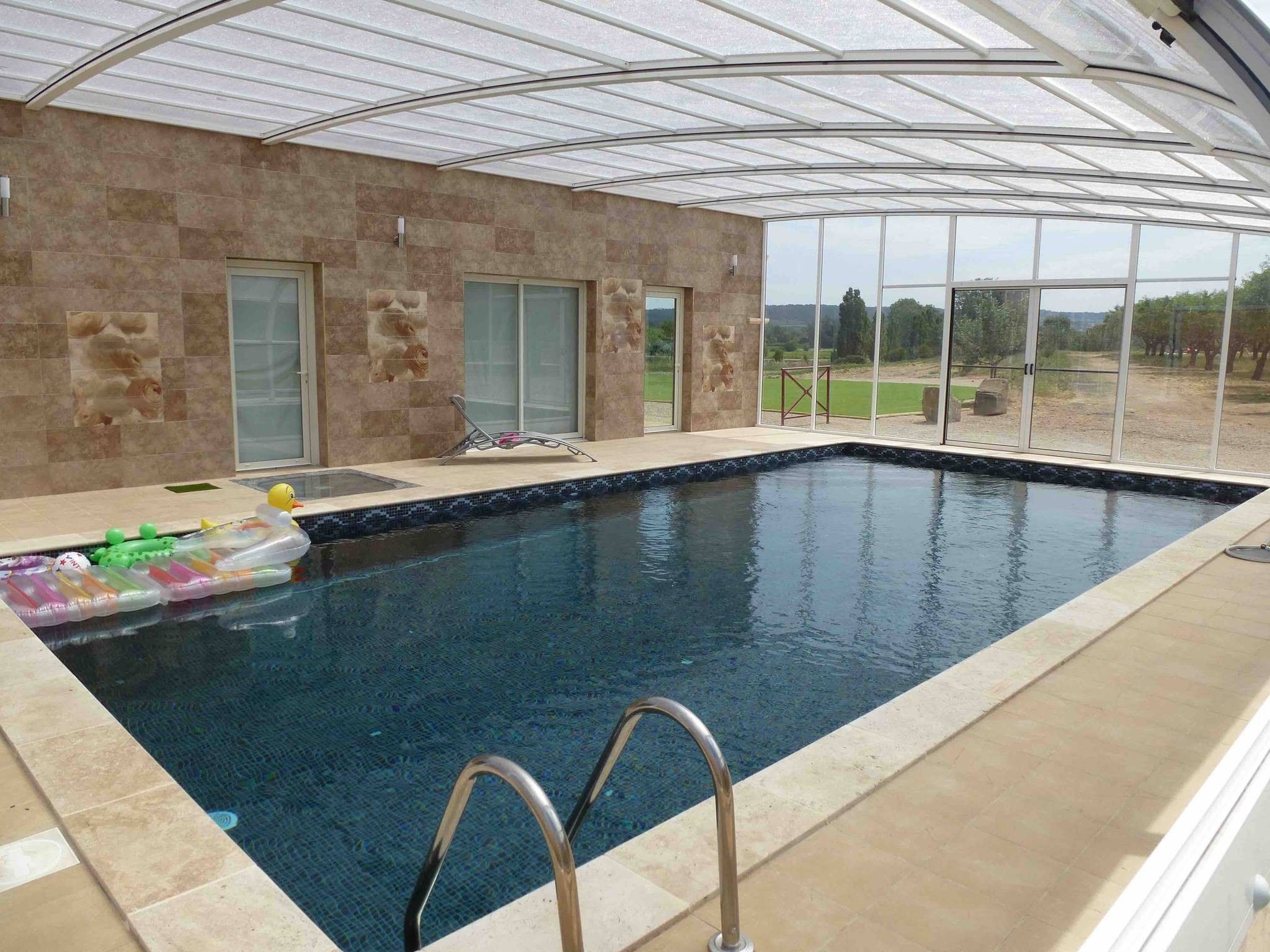 An indoor swimming pool with clear glass walls, a tiled floor, and a view of the outdoors.