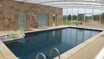 An indoor swimming pool with clear glass walls, a tiled floor, and a view of the outdoors.